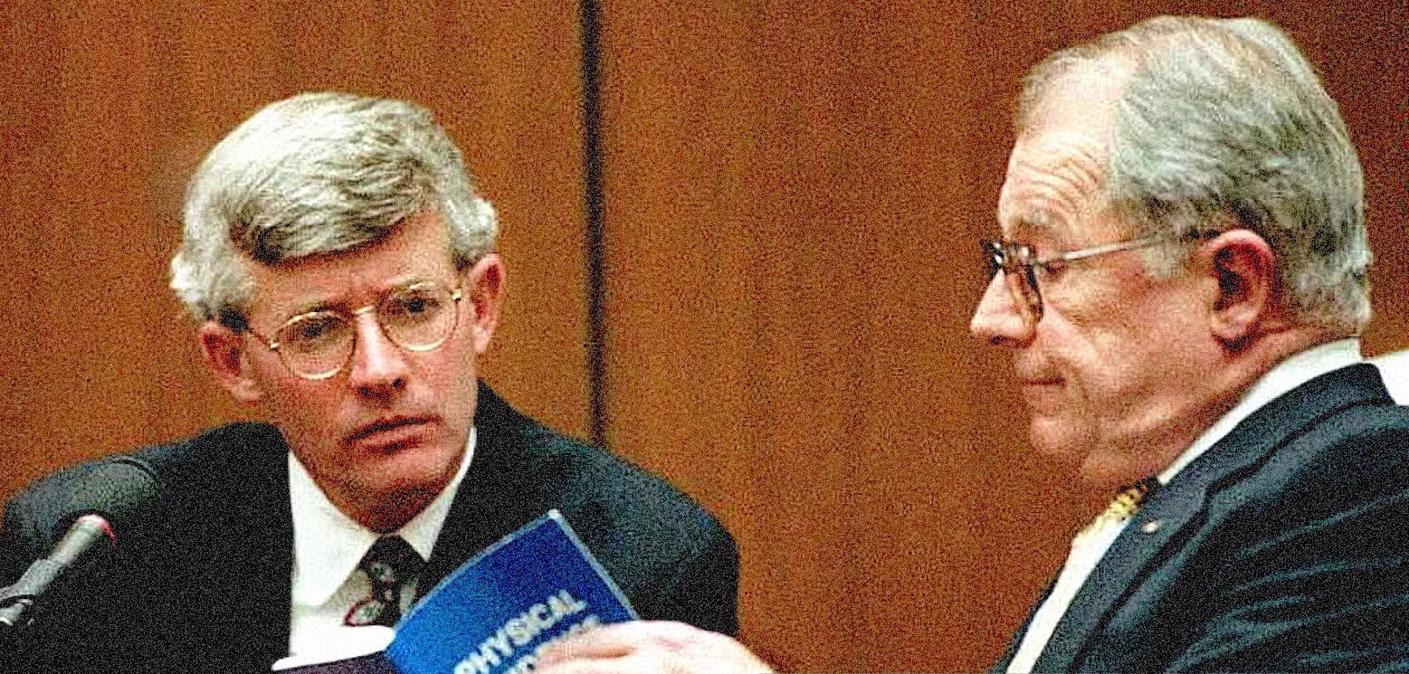A man testifying in court with a microphone and two older men listening, representing historical news, legal proceedings, and archival sound recordings.
