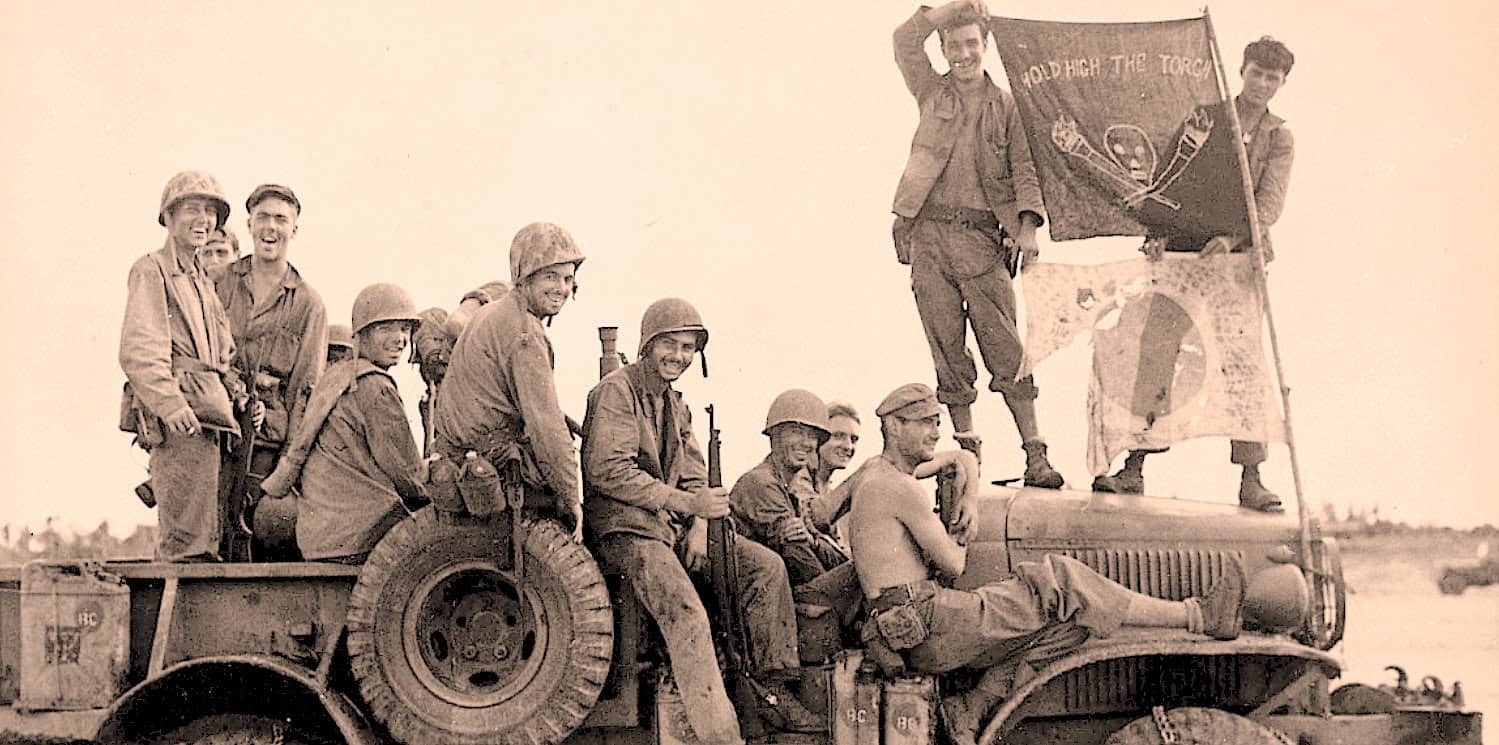 Soldiers celebrating on a military vehicle during World War II, holding flags and smiling, highlighting wartime camaraderie and victory moments; vintage black-and-white wartime photo.