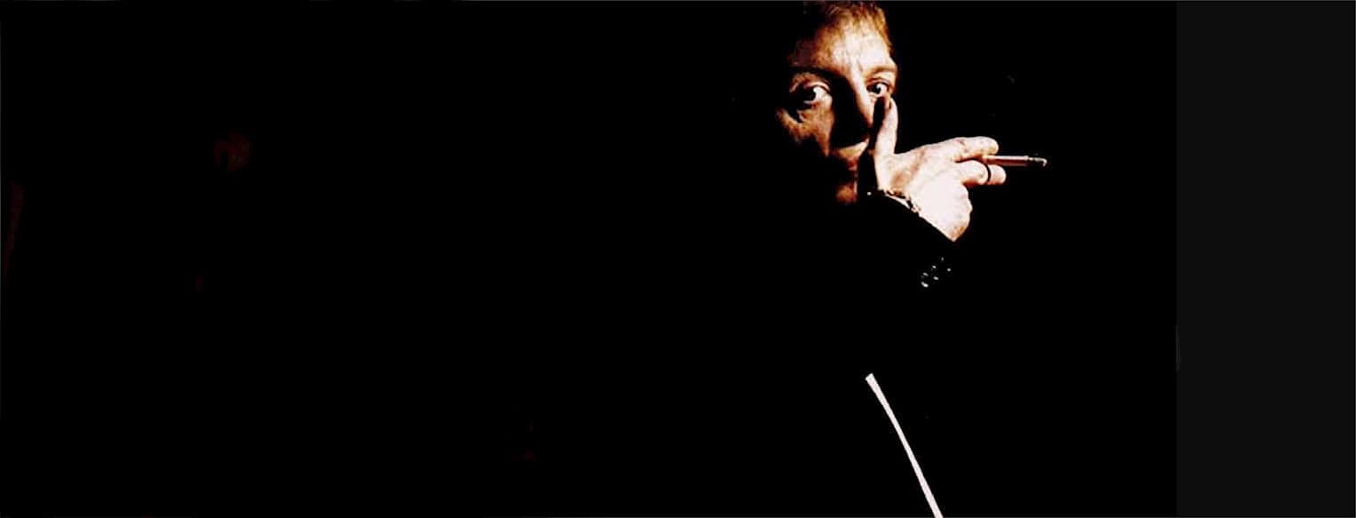 A vintage photo of a man smoking a cigarette with a dark background, representing historical news, music archives, and sound recordings from Past Daily.