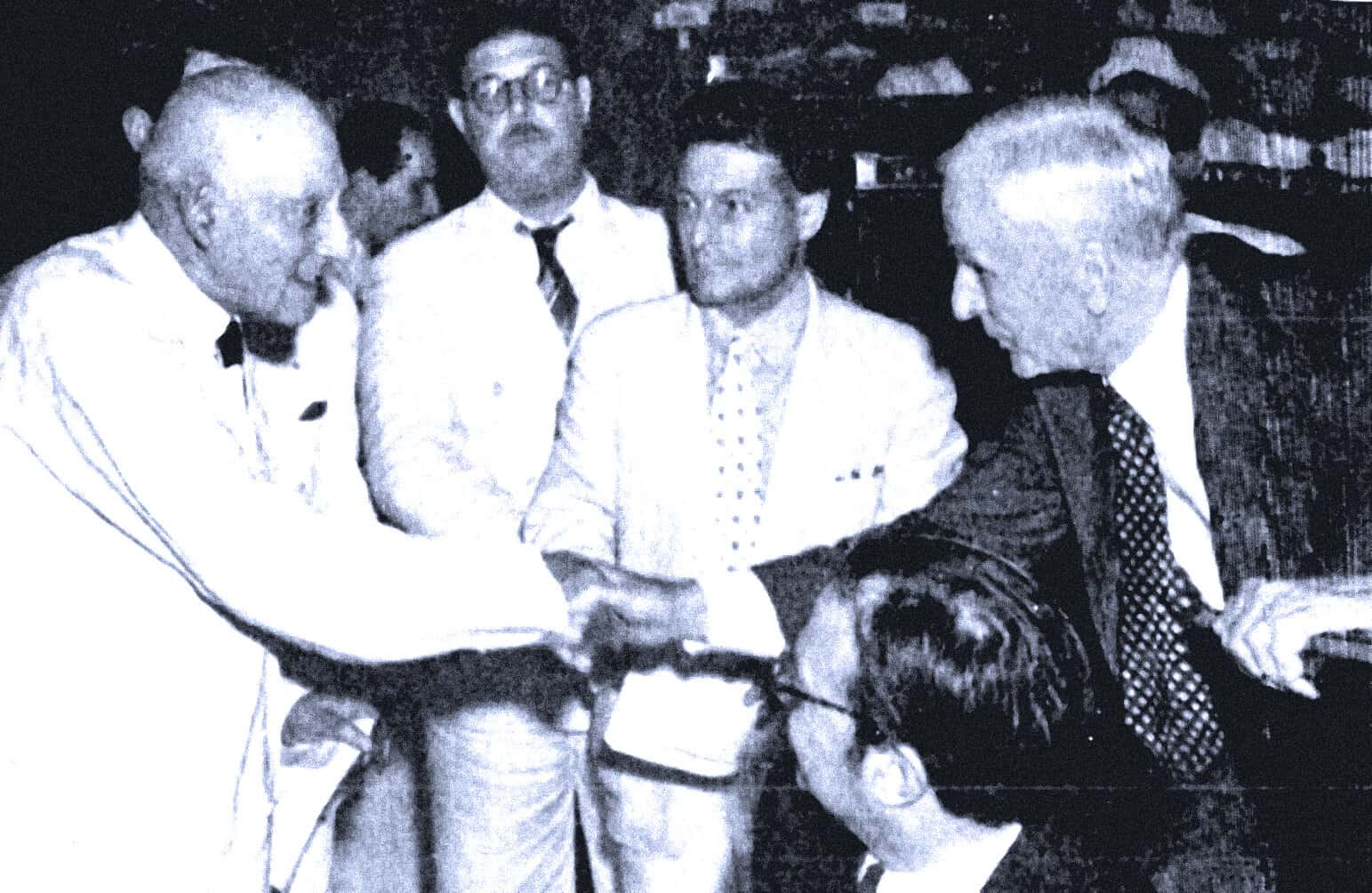 Shaking hands with a prominent political figure at a historical event, surrounded by men in formal attire recognizing a significant moment in history and news archives.