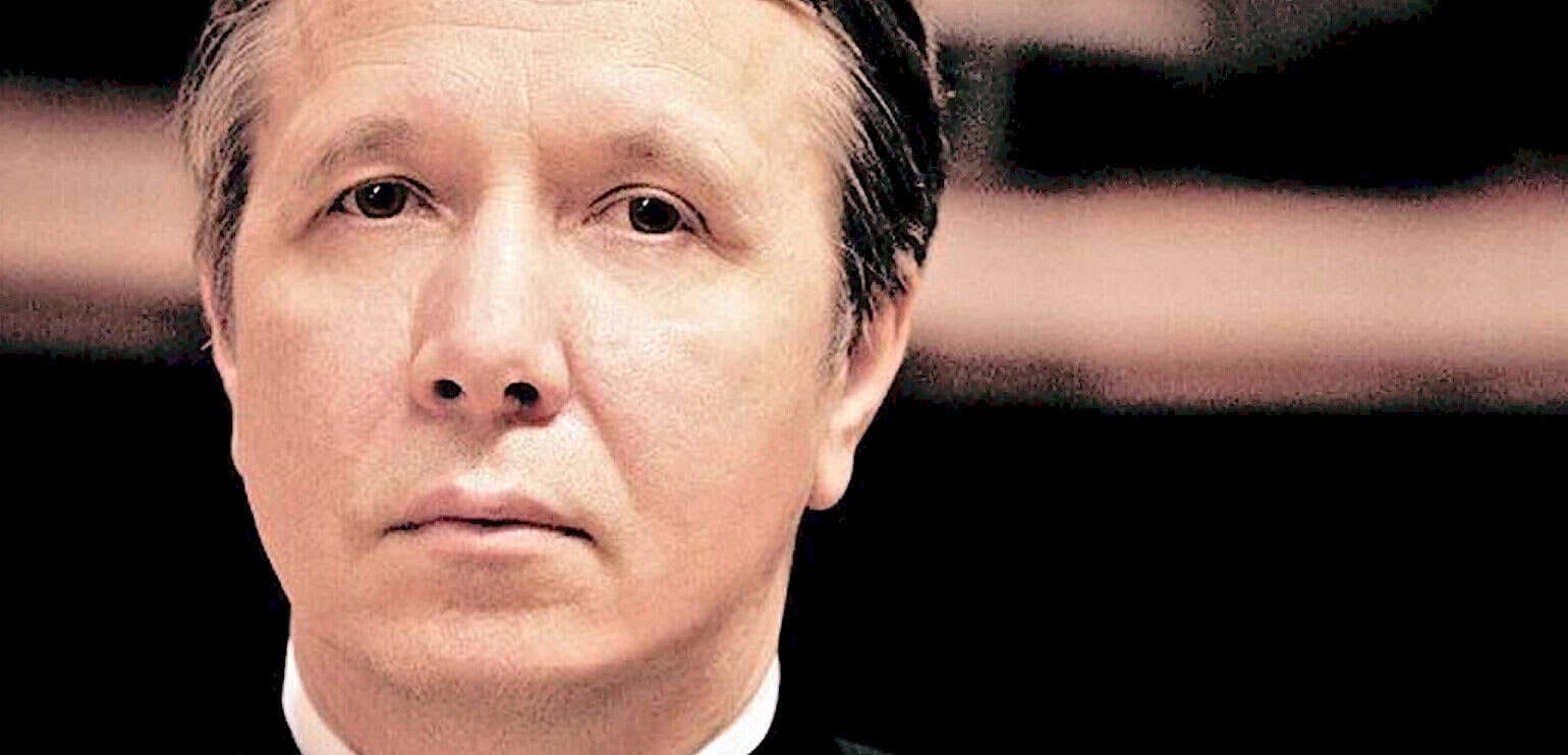 Close-up image of a man with Asian features, serious expression, formal attire, likely at a news or historical event, reflecting themes of news history and sound archives.