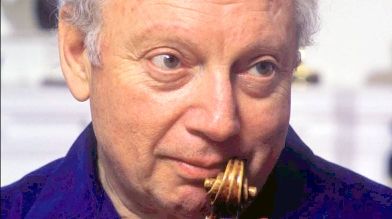 Close-up of a man with gray hair and blue eyes eating spaghetti, showcasing a humorous and candid moment.