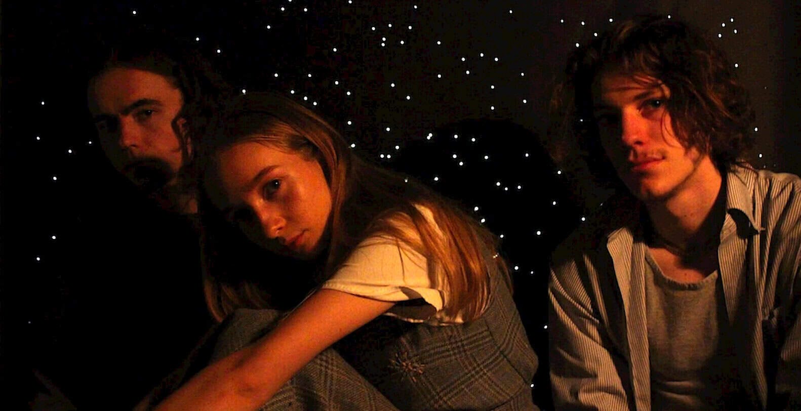 Shock with young people in vintage clothing, dark starry background, indie music scene, youthful fashion, alternative music vibe, nostalgic atmosphere, band members portrait, concert background, music lovers, nighttime performance, past daily archive.