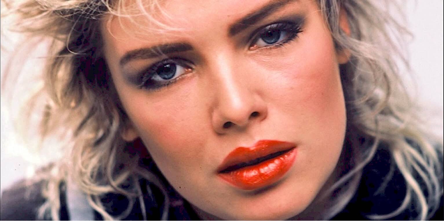 Close-up of a woman with blonde curly hair and striking blue eyes, showcasing vintage makeup look, emphasizing music, history, and nostalgic imagery for sound archives like Past Daily.
