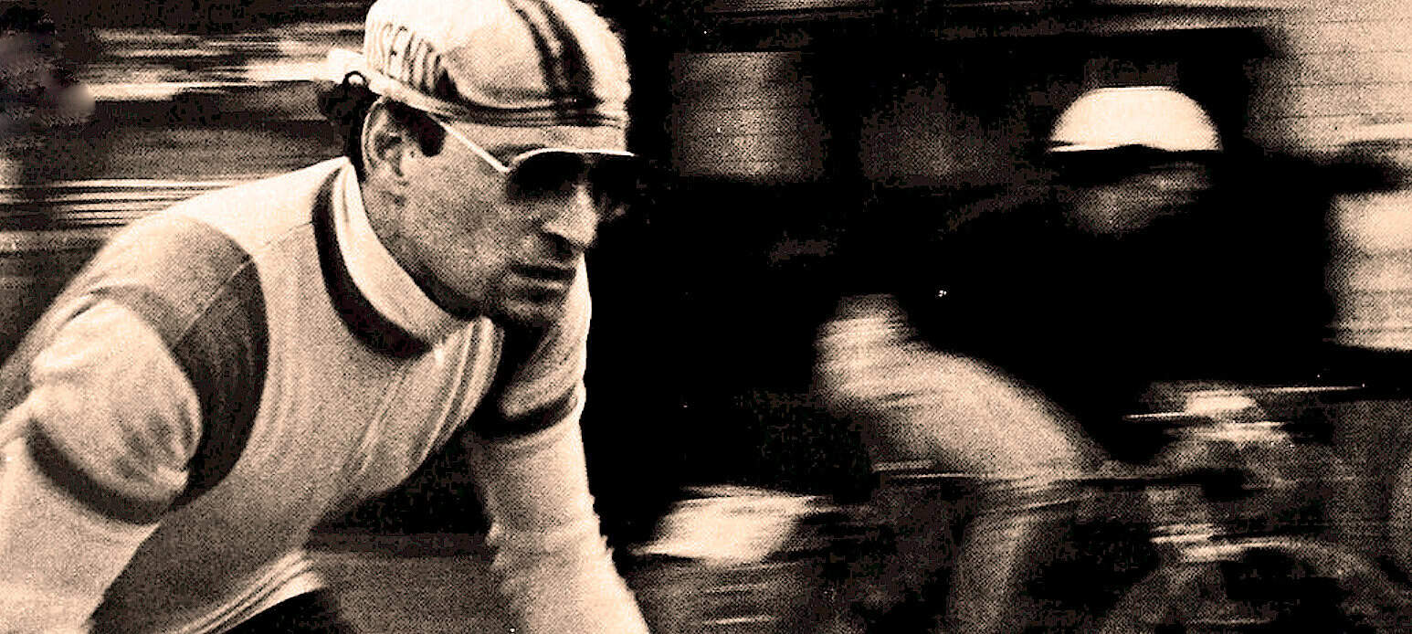 Cyclist wearing vintage racing gear and helmet, in motion during a race, representing classic sports and historical cycling events, related to vintage sports archives.