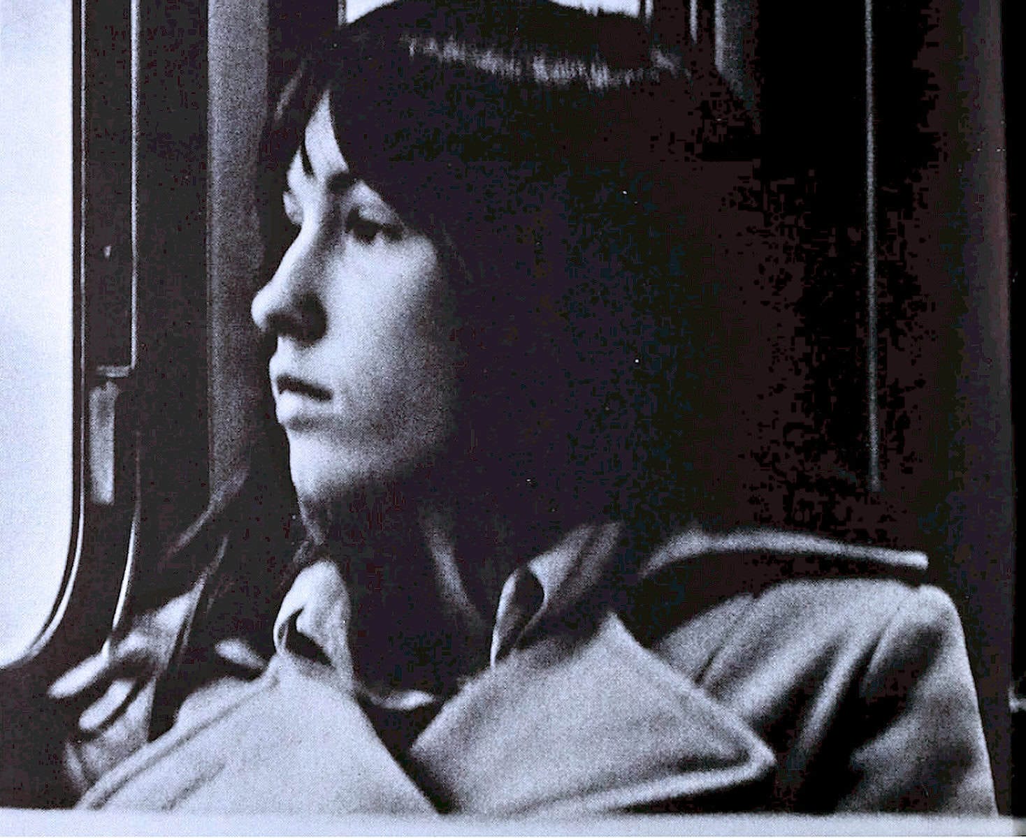 A young woman looking out a window, in black and white, capturing a reflective moment perfect for vintage music and history archives.