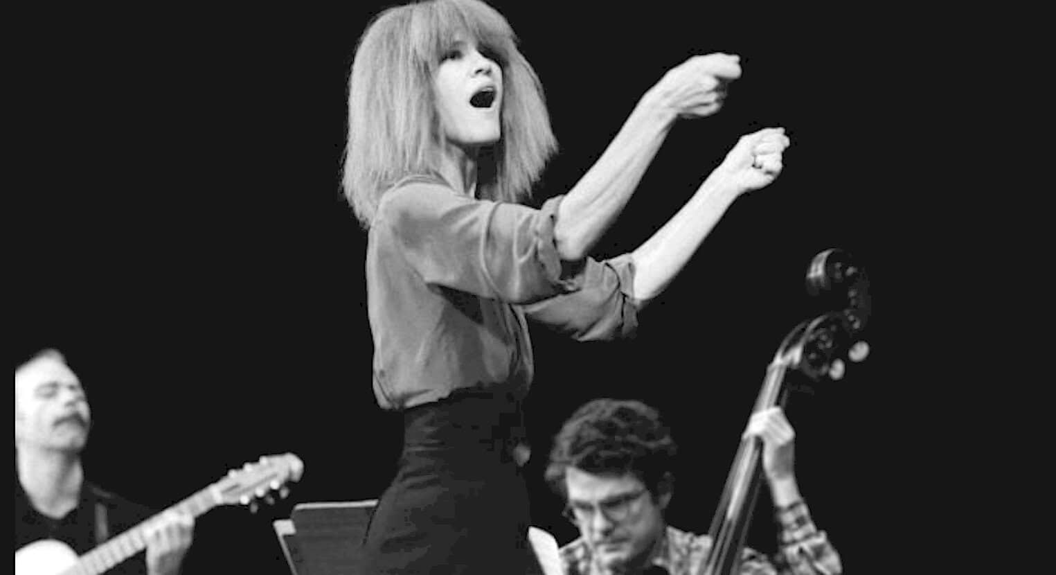 Archive photo of a female jazz singer performing with musicians on stage, black and white image emphasizing music, history, and live performances, perfect for past daily sound archive content.