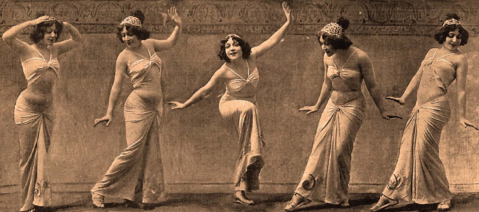 Elegant vintage women dancers performing traditional dance with flowing dresses, sepia tone, 1920s era, entertainment, artistic expression, historical dance performance, classic stage setting.