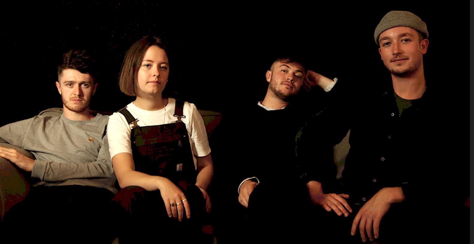 Young indie band sitting on a dark background, showcasing modern music culture and sound archive relevance.