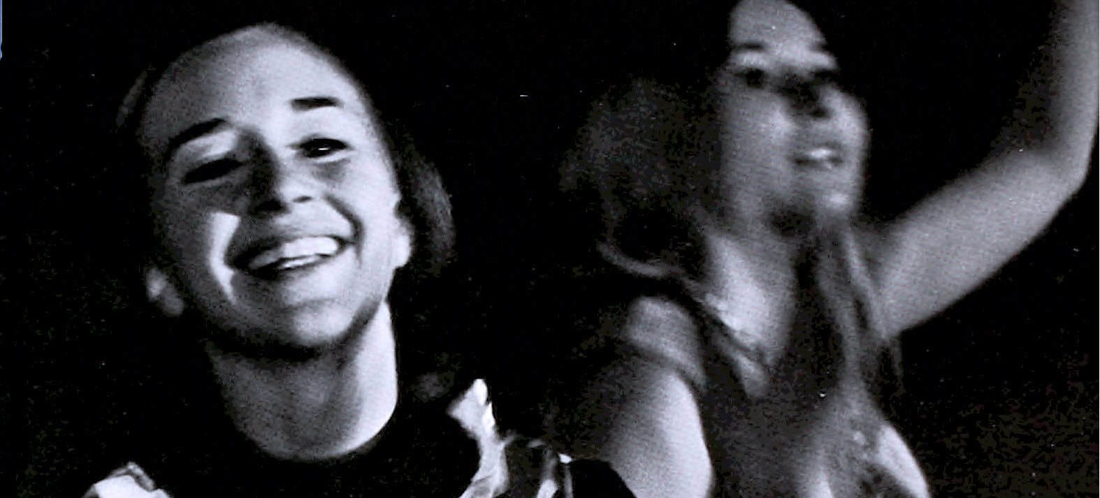 Smiling woman and woman with headphones enjoying music in a black and white photo, capturing moments of joy and live audio experience.