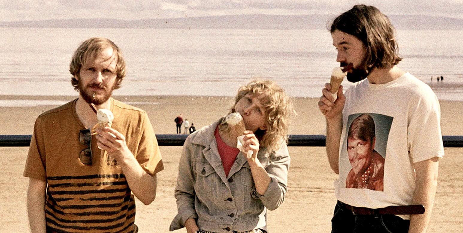Beach scene with three friends enjoying ice cream during sunset, casual summer day, vintage style, relaxed atmosphere, friends having fun at the seaside, 80s fashion, nostalgic summer vibe, ocean background, shared moment of joy, ice cream love, free-spirited travel, scenic sky, joyful gathering, memory making, leisure and recreation.