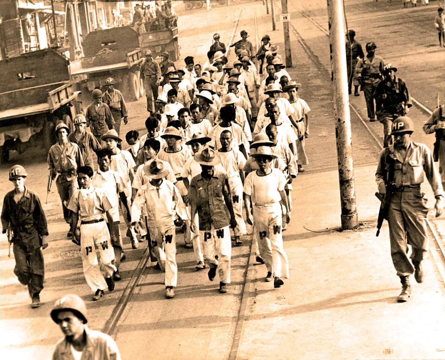 A historic black-and-white photo of soldiers crossing a city street during wartime, with police officers and tram tracks, representing military history, wartime news, and historical archives.