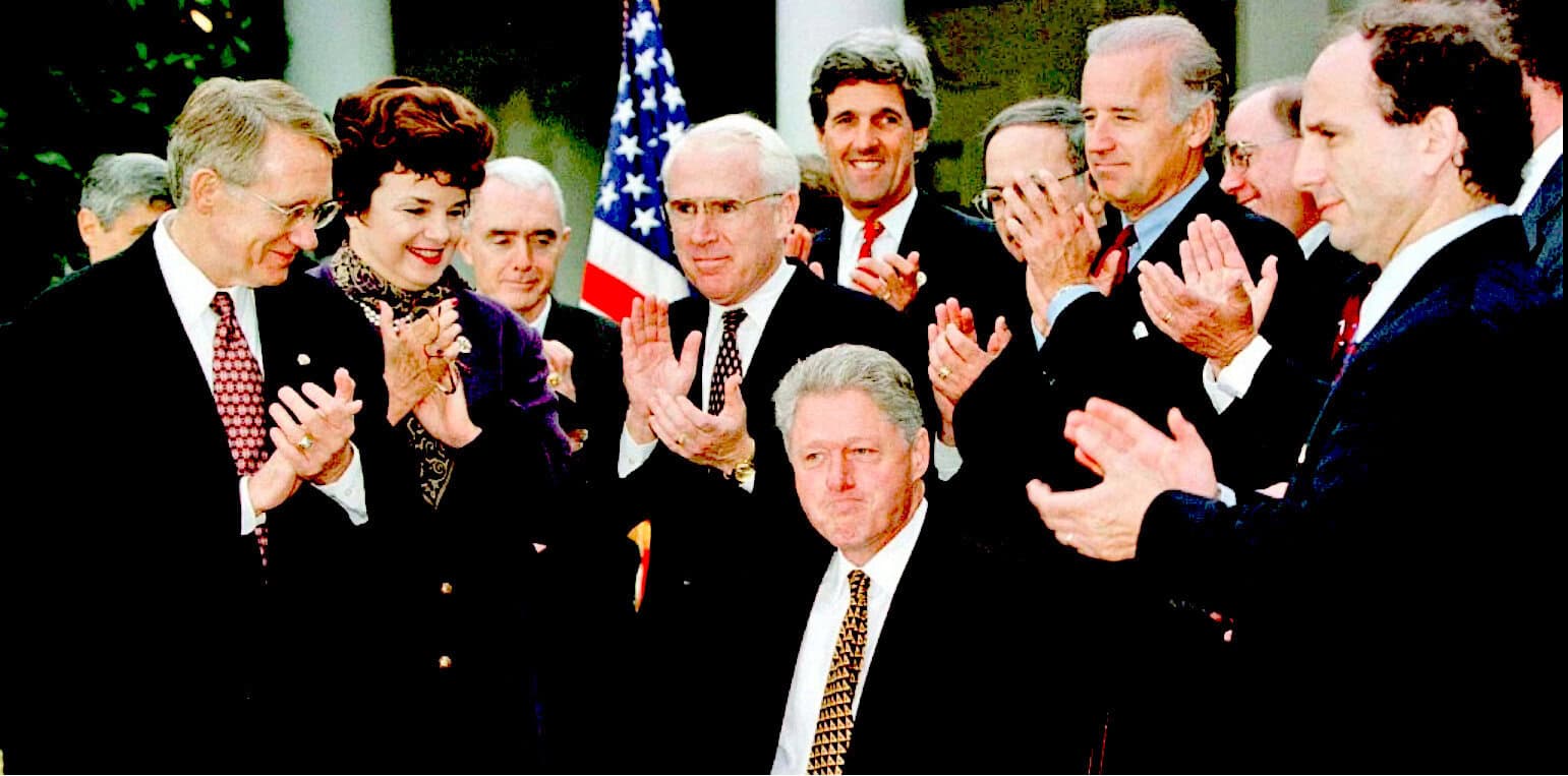 People of different ages celebrating and clapping together at a formal event with an American flag in the background, illustrating historical or political significance.