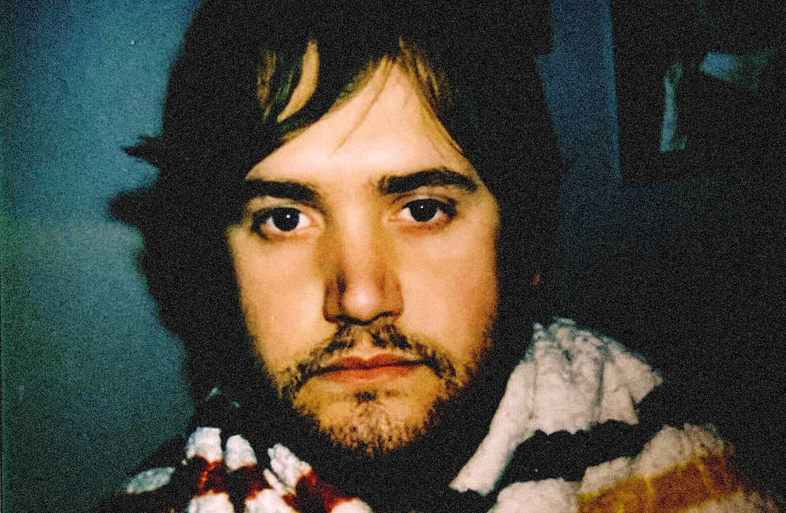 Young man with dark hair and beard, looking directly at the camera, in a close-up portrait emphasizing his facial features.