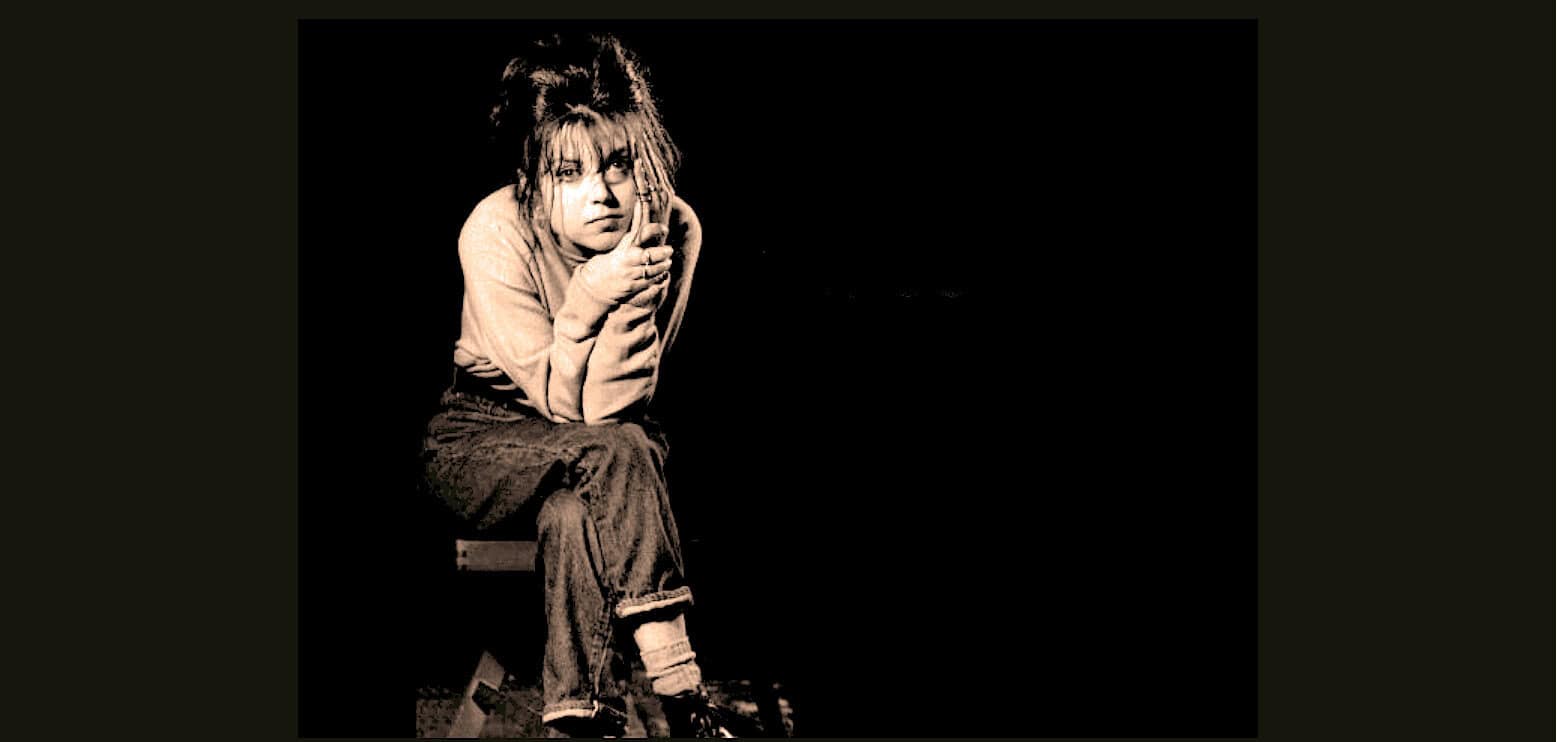 Grunge musician Kurt Cobain sitting on a stool, wearing casual clothing, with a contemplative expression, black background, iconic image of 90s alternative rock.