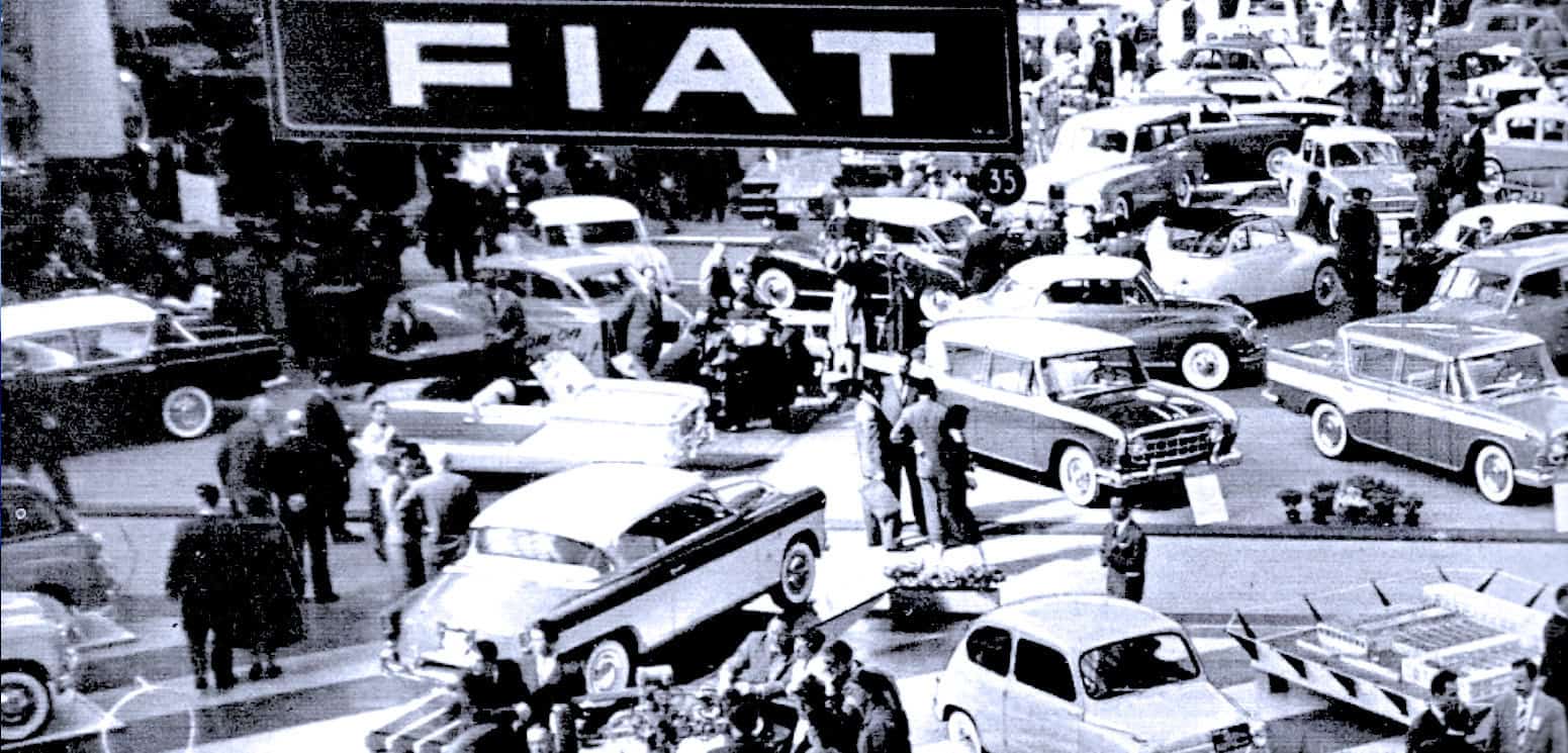 Vintage car show at Fiat dealership with classic automobiles and visitors, capturing historic automotive industry moments.