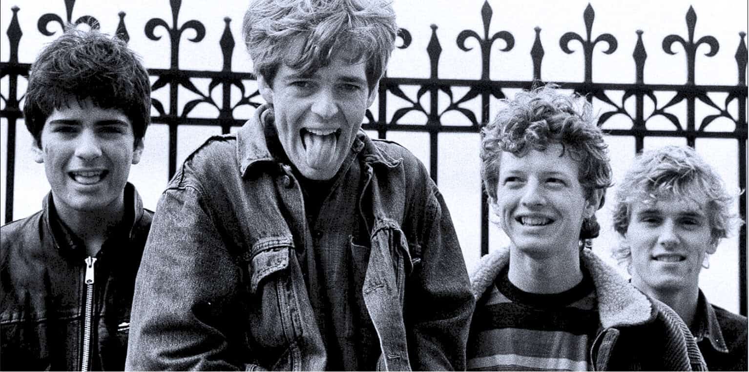 The Beatles, iconic rock band, in a candid black and white photo with playful expressions, standing outdoors in front of a wrought iron fence, representing music history and youth culture.