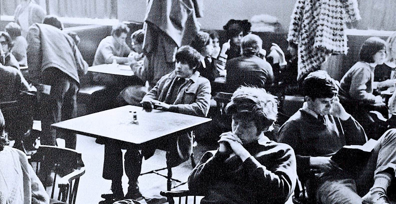 Historic black and white photo of people in a music listening room, capturing a moment of communal listening, with vintage seating and acoustic setup, representing past music and radio history.