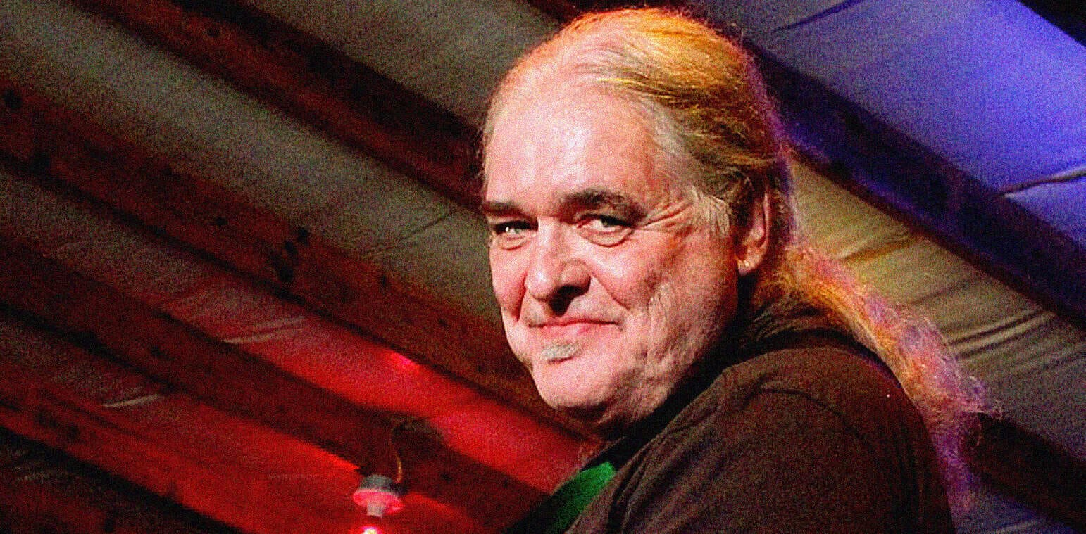 Vintage rock musician with long blond hair, performing at a live music event captured in a vibrant, colorful setting.