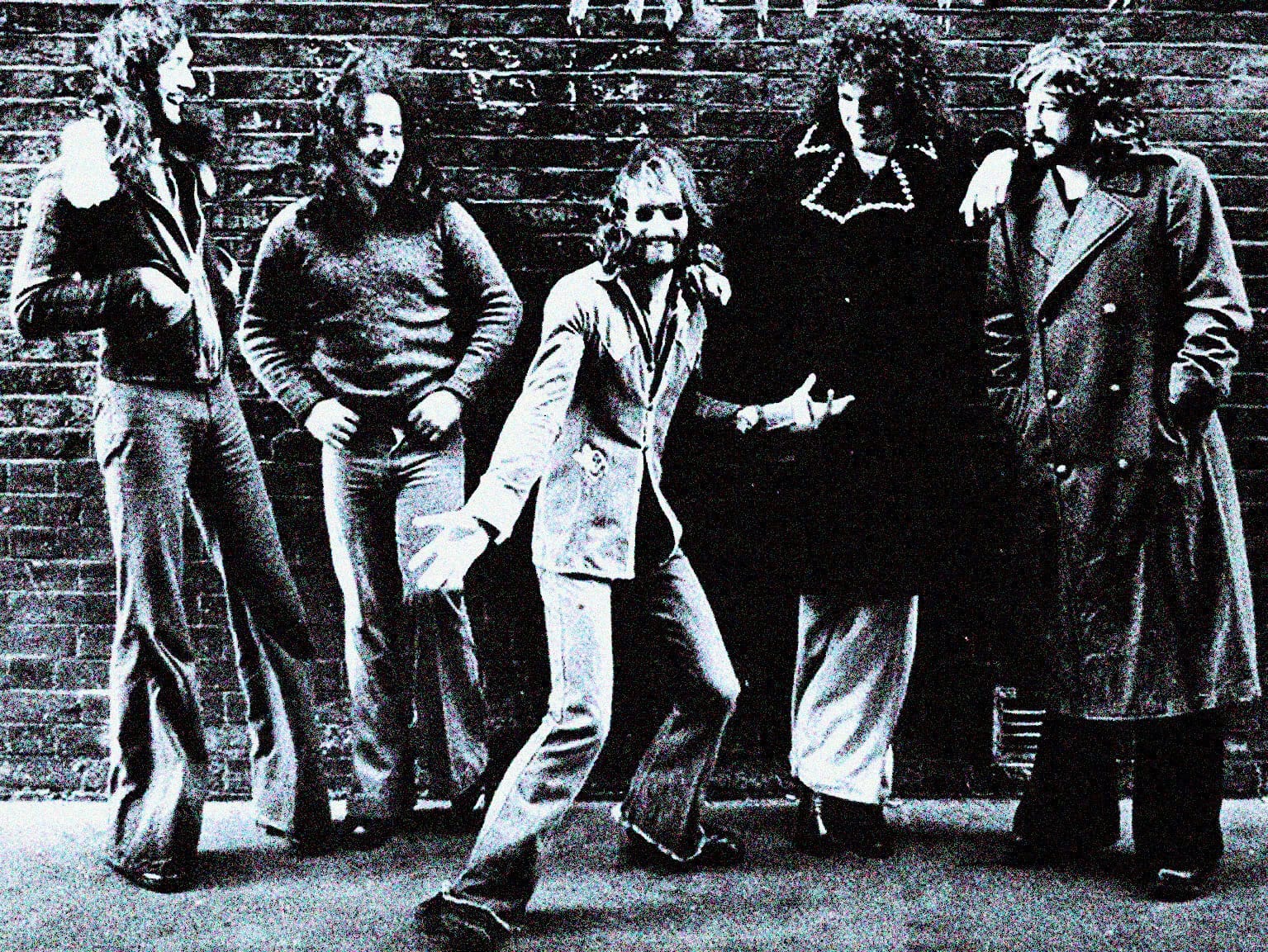 Urban music band posing against a brick wall, showcasing late 20th-century rock and alternative style, emphasizing music history and culture.
