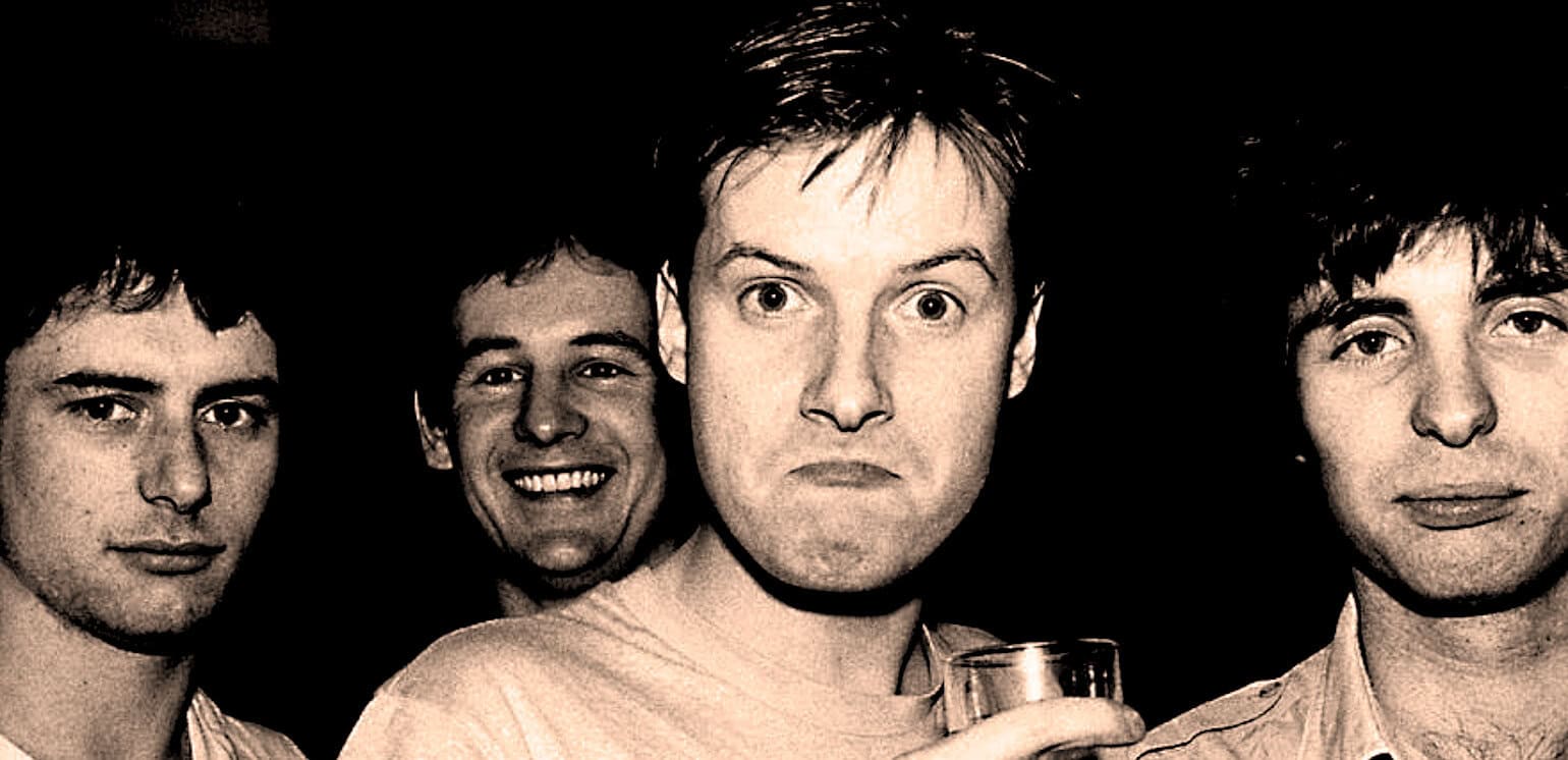 Black and white photo of four young men with expressive faces at a music or news event, showcasing a band or group associated with past daily sound archive of news, history, and music.