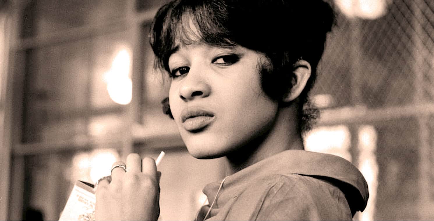 Vintage black and white photo of a woman with short hair holding a cigarette, representing historical news, music, or cultural archives on Past Daily.