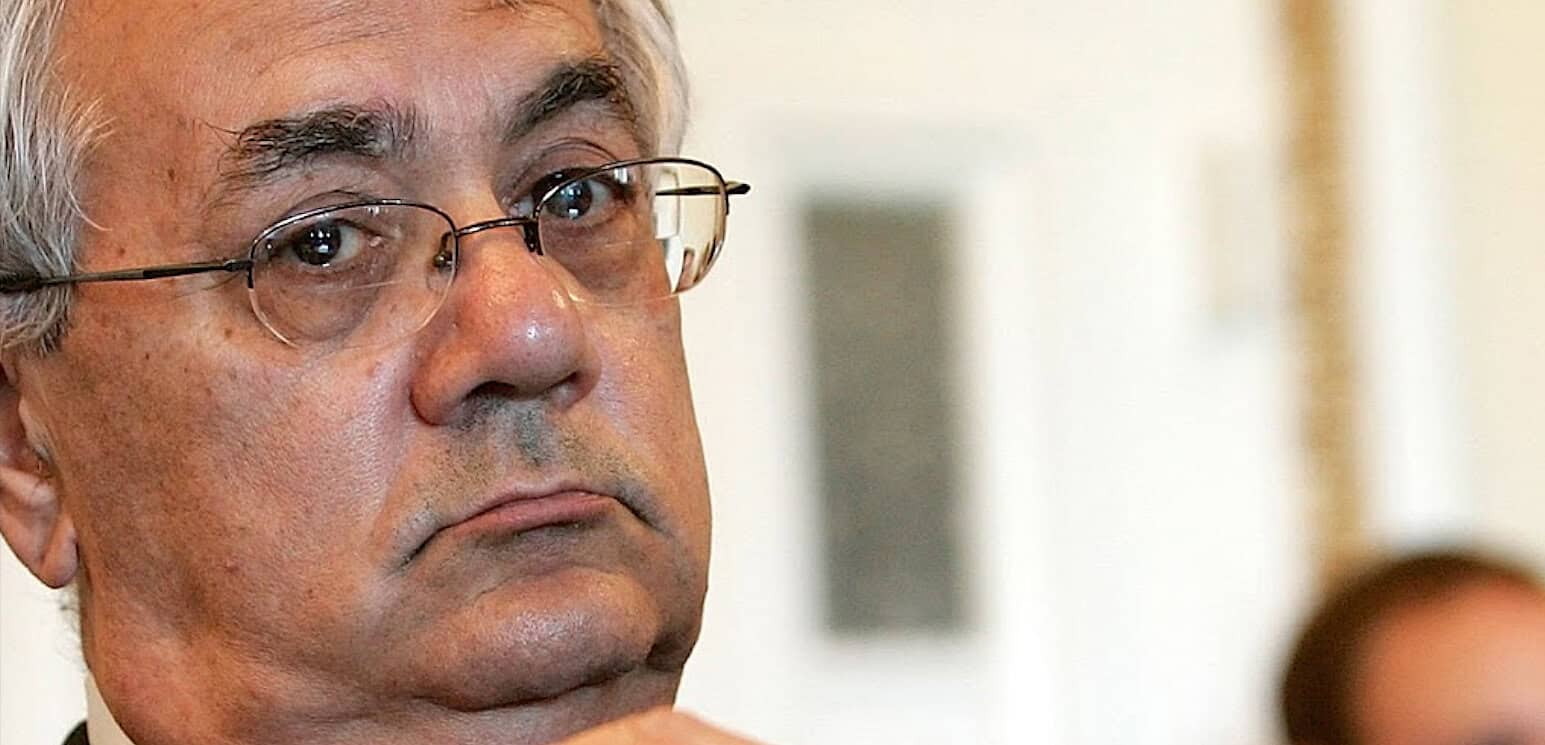 Thoughtful senior man wearing glasses listening attentively at a news or history event.