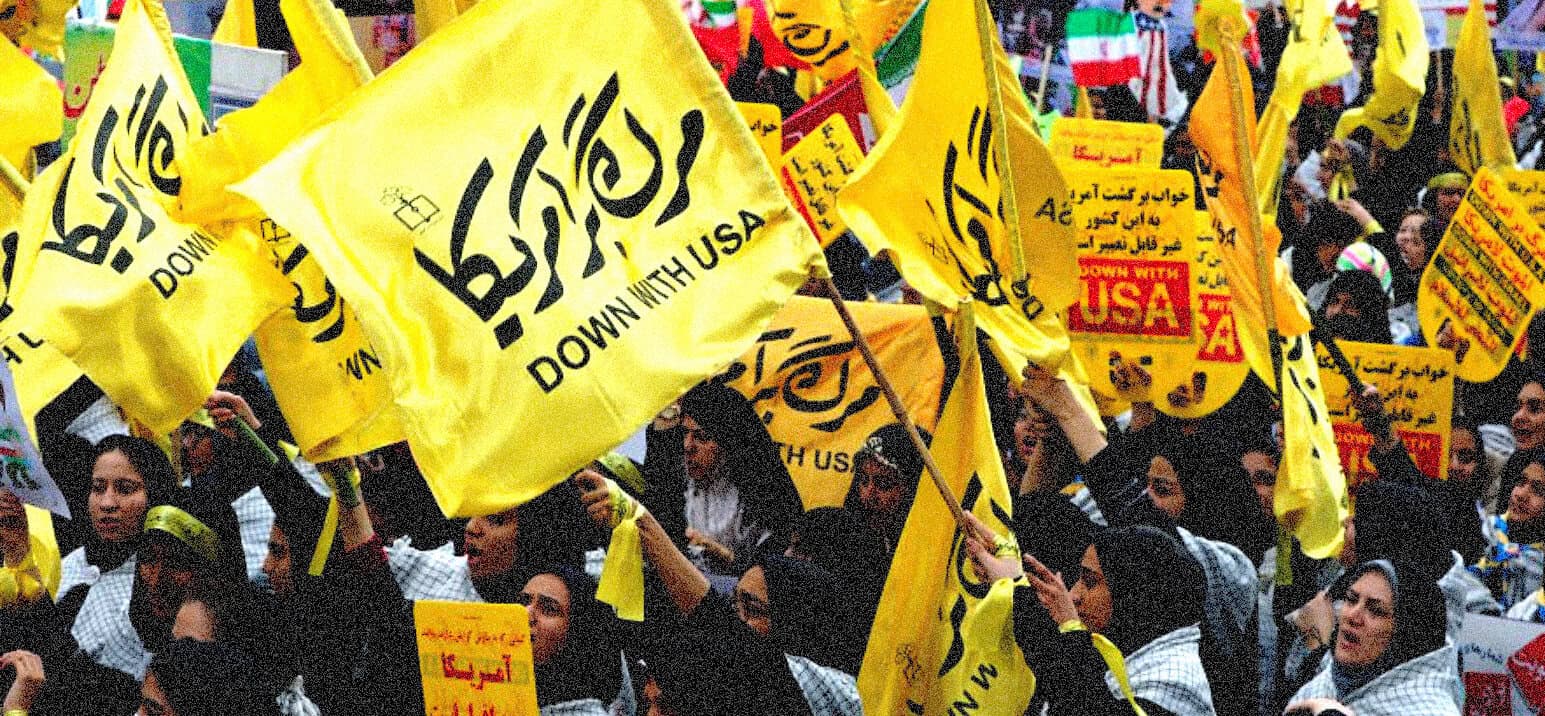Yellow flags with black Arabic text and "DOWN WITH USA" slogans at a protest or rally in a crowd of people.