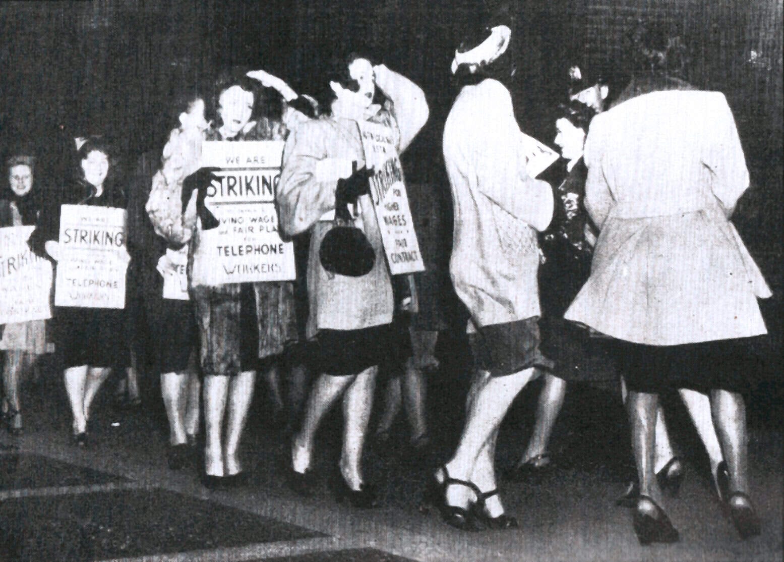 Women protestor holding a sign during a women's rights demonstration, advocating for fair pay and better working conditions, with others holding signs in the background.