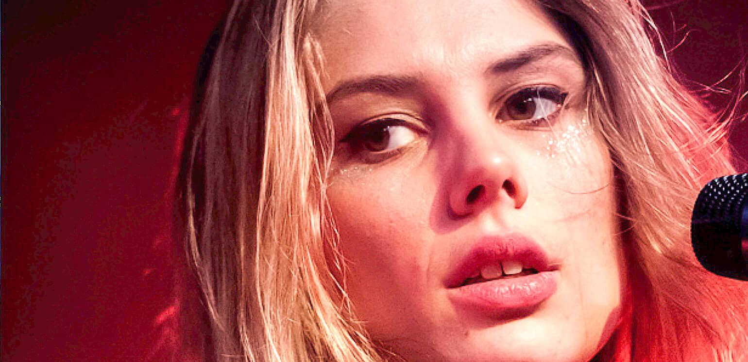 Close-up of a female singer with blonde hair performing with a microphone at a music event, highlighting her expressive face and emotional connection to the music.