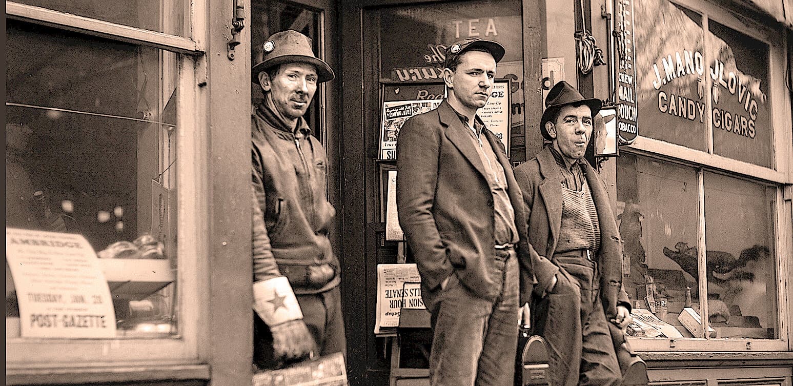 A vintage black and white photo of three men standing outside a store with signs for candy, cigars, and other goods, capturing a historic scene with nostalgic and cultural significance.