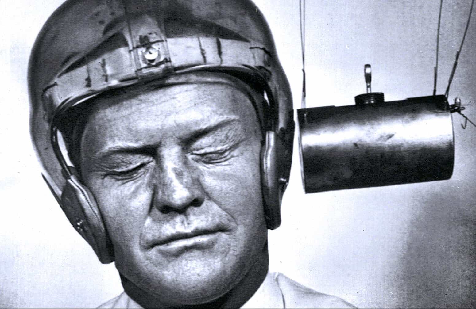 Vintage radio broadcasting engineer wearing headphones and a hard hat during a live news or music broadcast. Black and white photograph capturing mid-20th century radio transmission history.