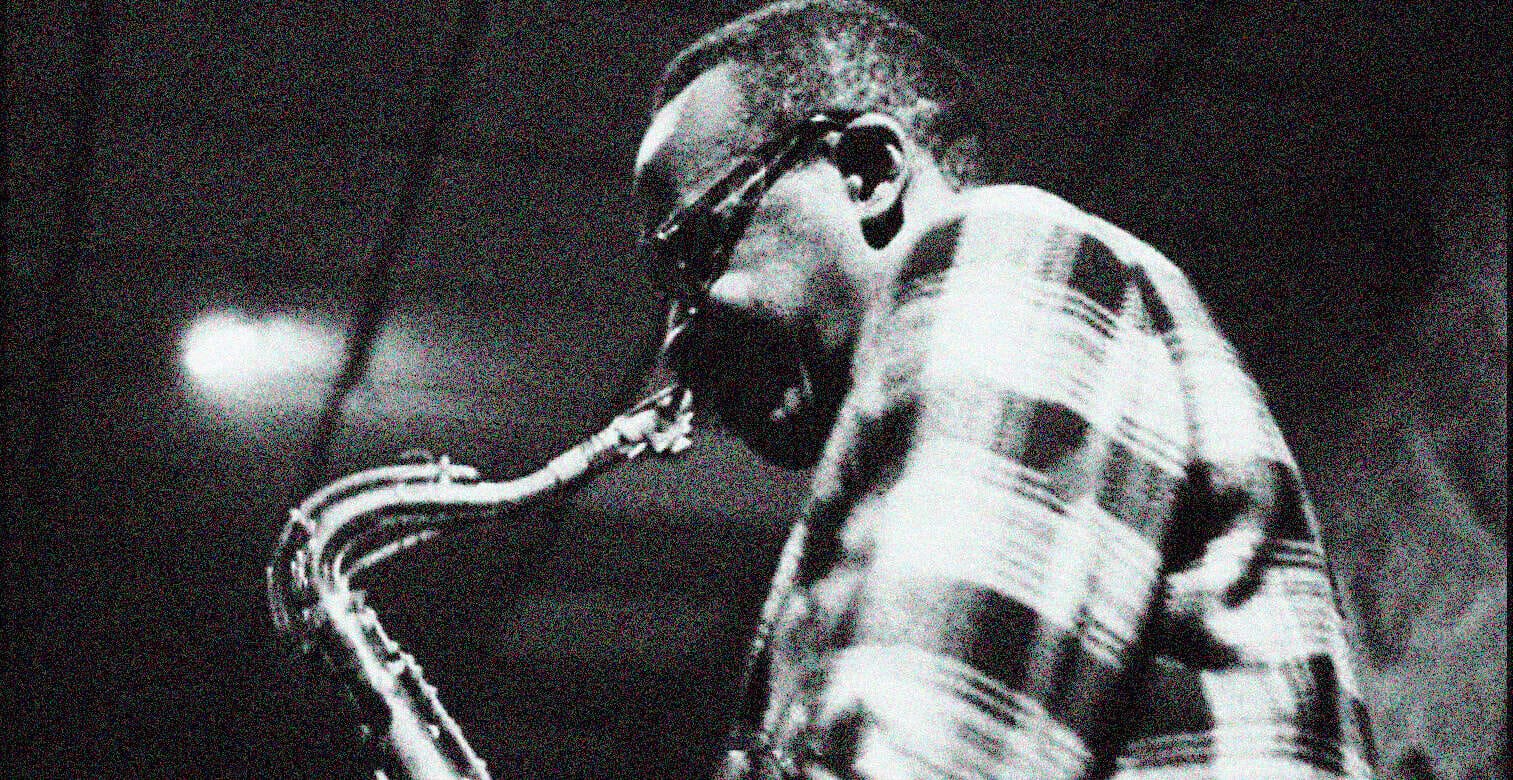 Vintage jazz saxophonist with sunglasses, playing saxophone, black and white photo, music history, iconic music scene, jazz musician, music archive, classic jazz, black and white photography, musical performance.