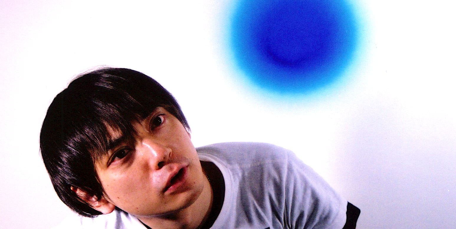 Headshot of young Asian man with black hair, casual t-shirt, minimalist background, blue circular art, modern portrait, youth culture, contemporary photography, genre of music and news archive.