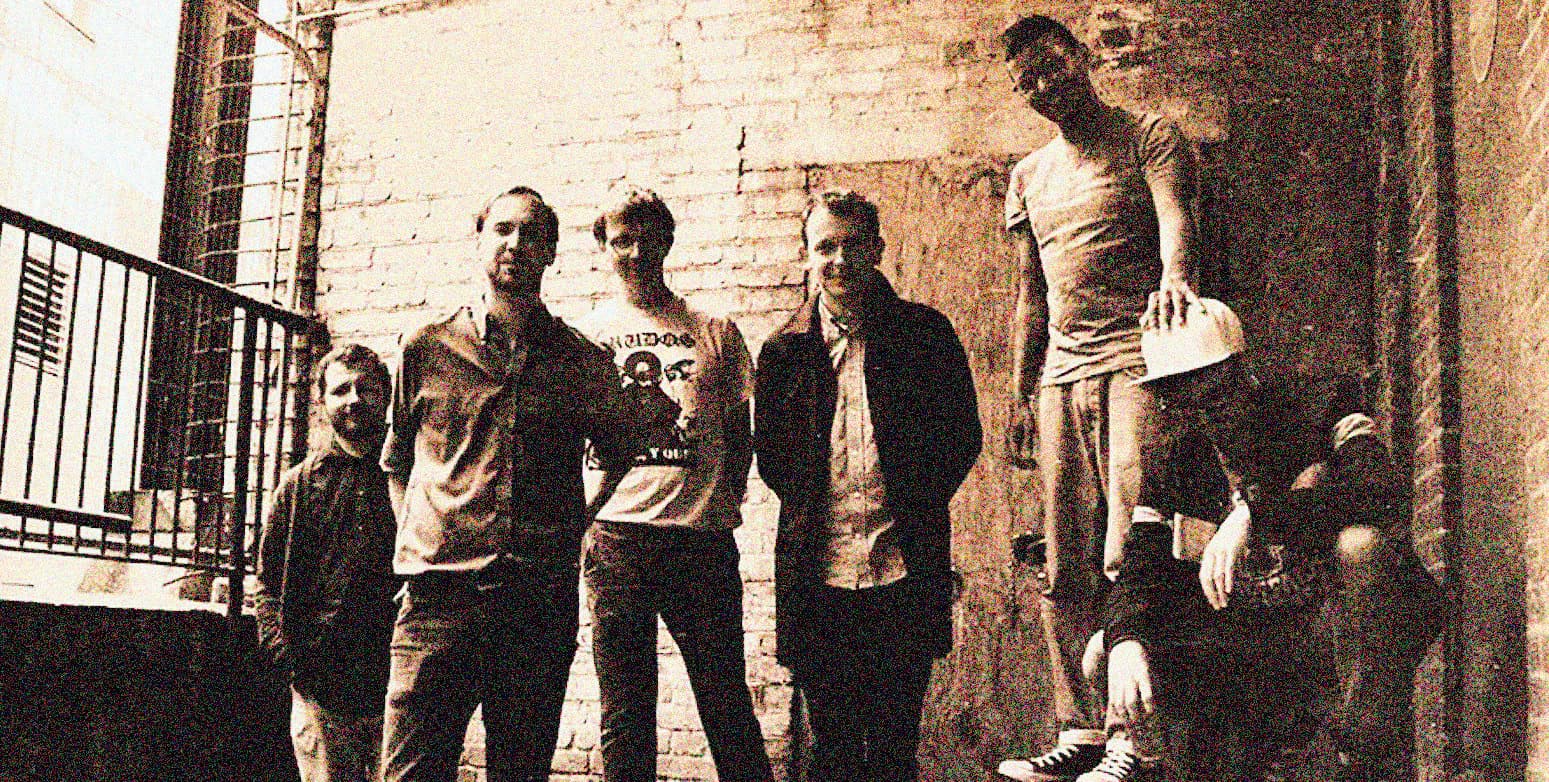 Vintage black-and-white photo of a diverse group of young people standing against a brick wall, capturing the essence of musical history, news, and cultural moments for Past Daily archival content.
