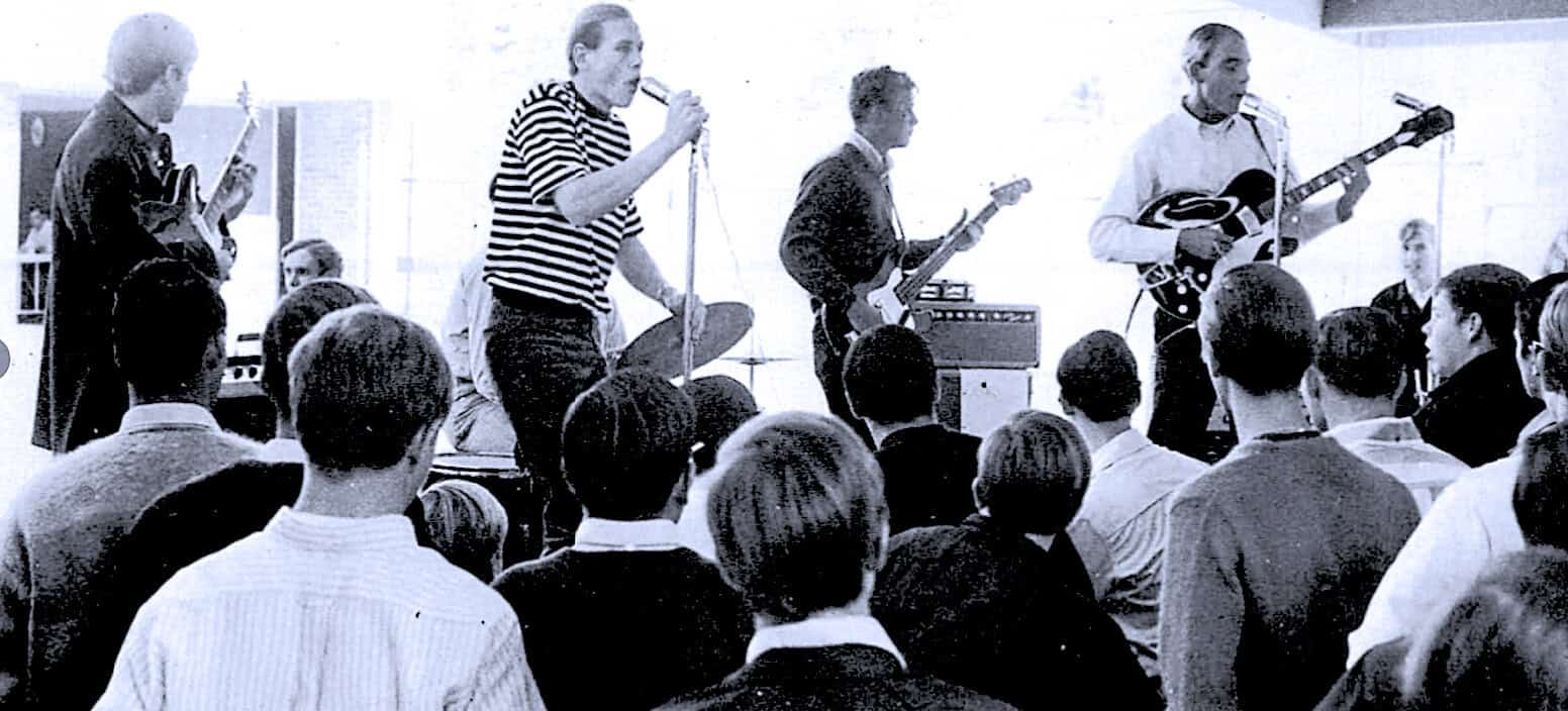 Vintage black and white photo of a 1950s rock band performing live in front of an audience, showcasing classic guitars, band members, and retro stage setup.