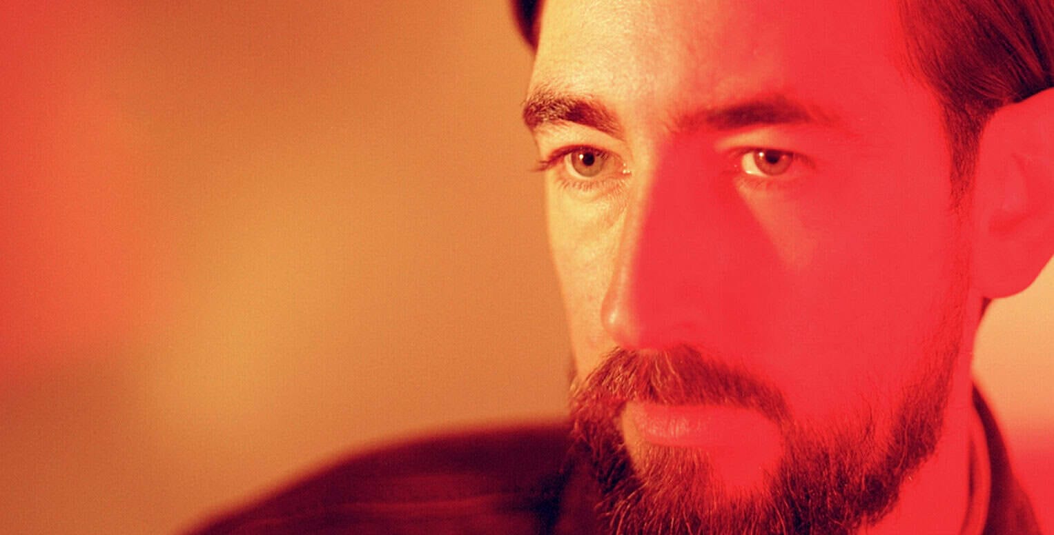 Historic man with a beard and intense gaze, close-up portrait, warm red and yellow lighting, expressive look, vintage style, photo related to news, history, and music archives, Past Daily sound archive.
