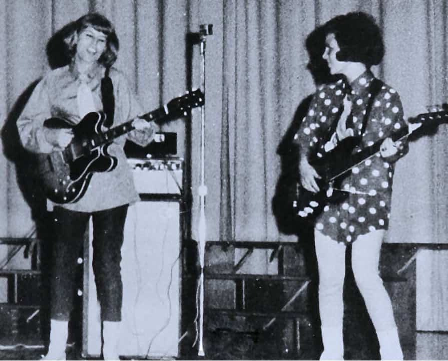 A black and white photo of two female musicians performing with guitars on stage, capturing a vintage music scene.