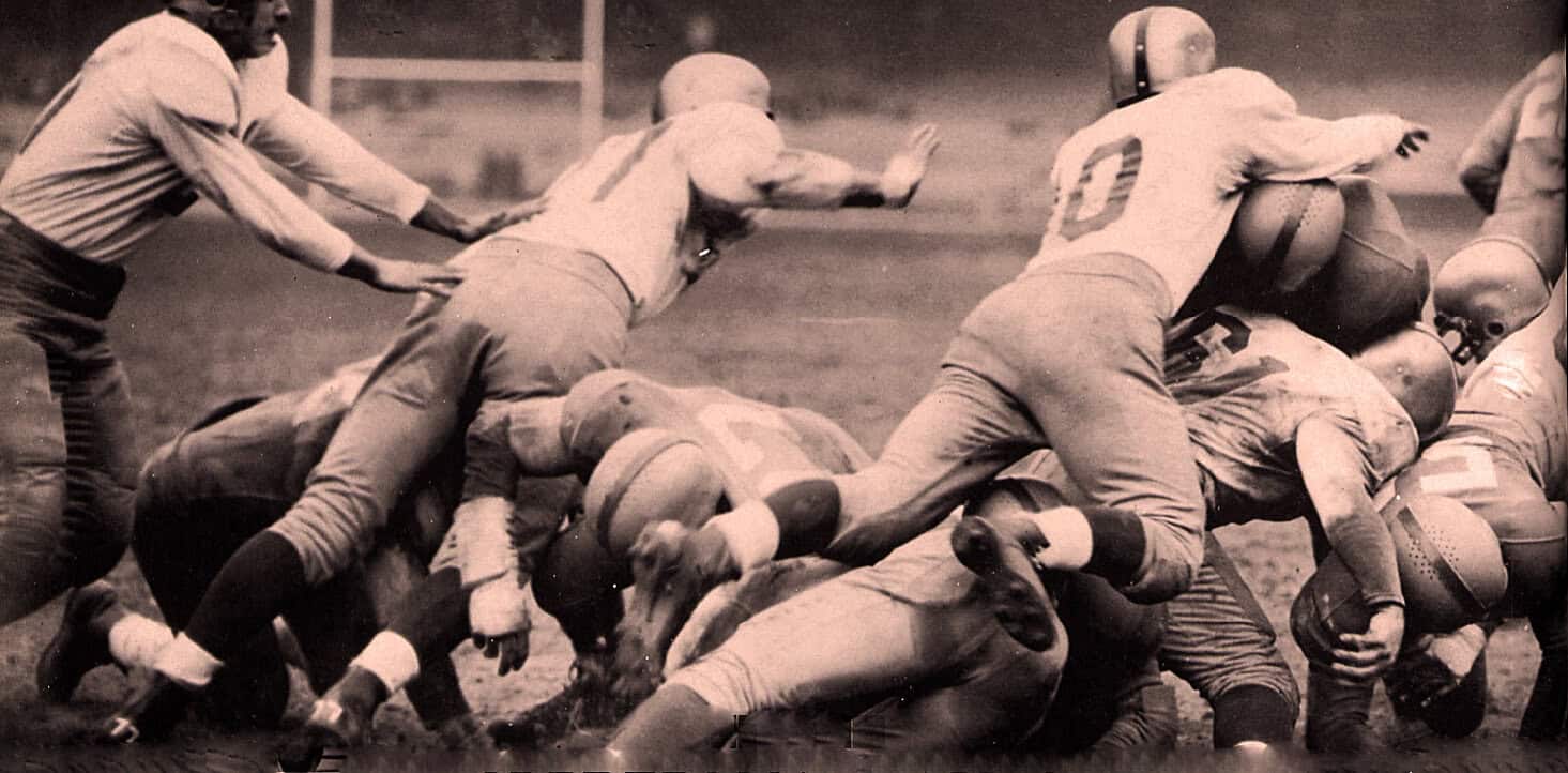 Football players tackling during a game in vintage black-and-white photograph, capturing action, sports history, and American football INA sports archive, illustrating athletic competition and team dynamics.