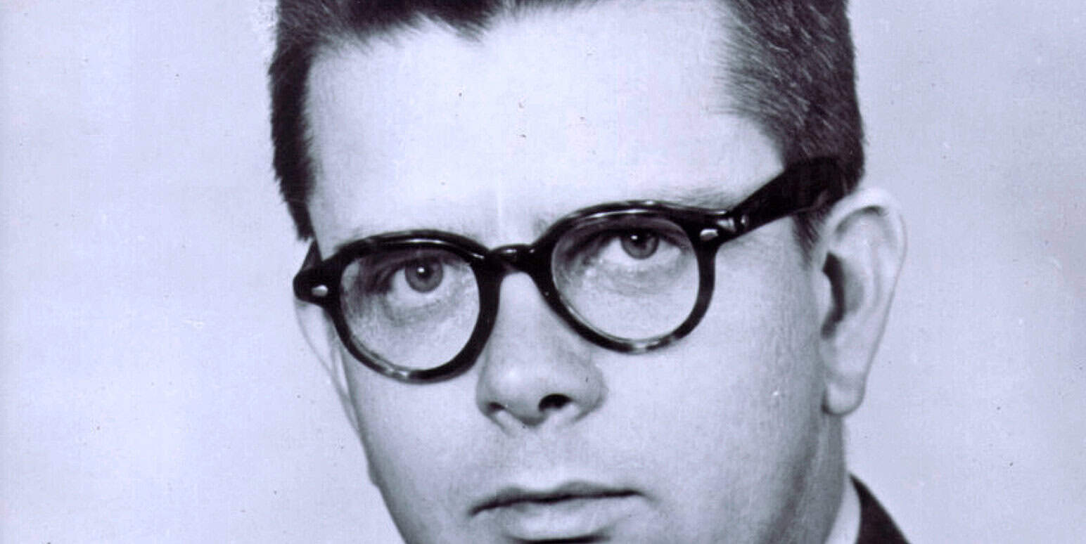 Vintage black and white photo of a man wearing round glasses, highlighting historical news and music archives.