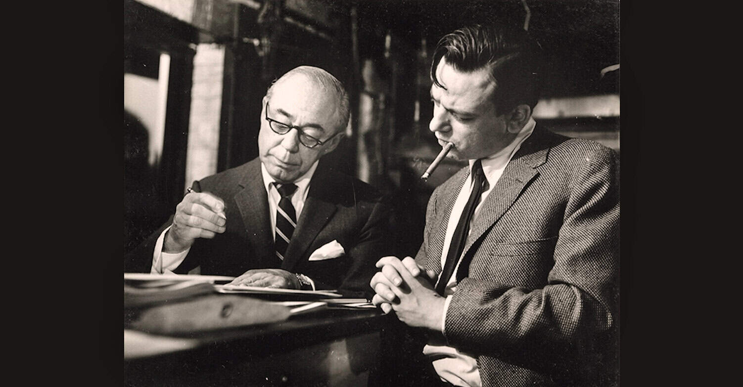 Man and older man in suit with cigarette, historical black and white photo, radio or news archive, vintage interview scene, classic media history, vintage journalism, black-and-white photography, mid-20th century media.