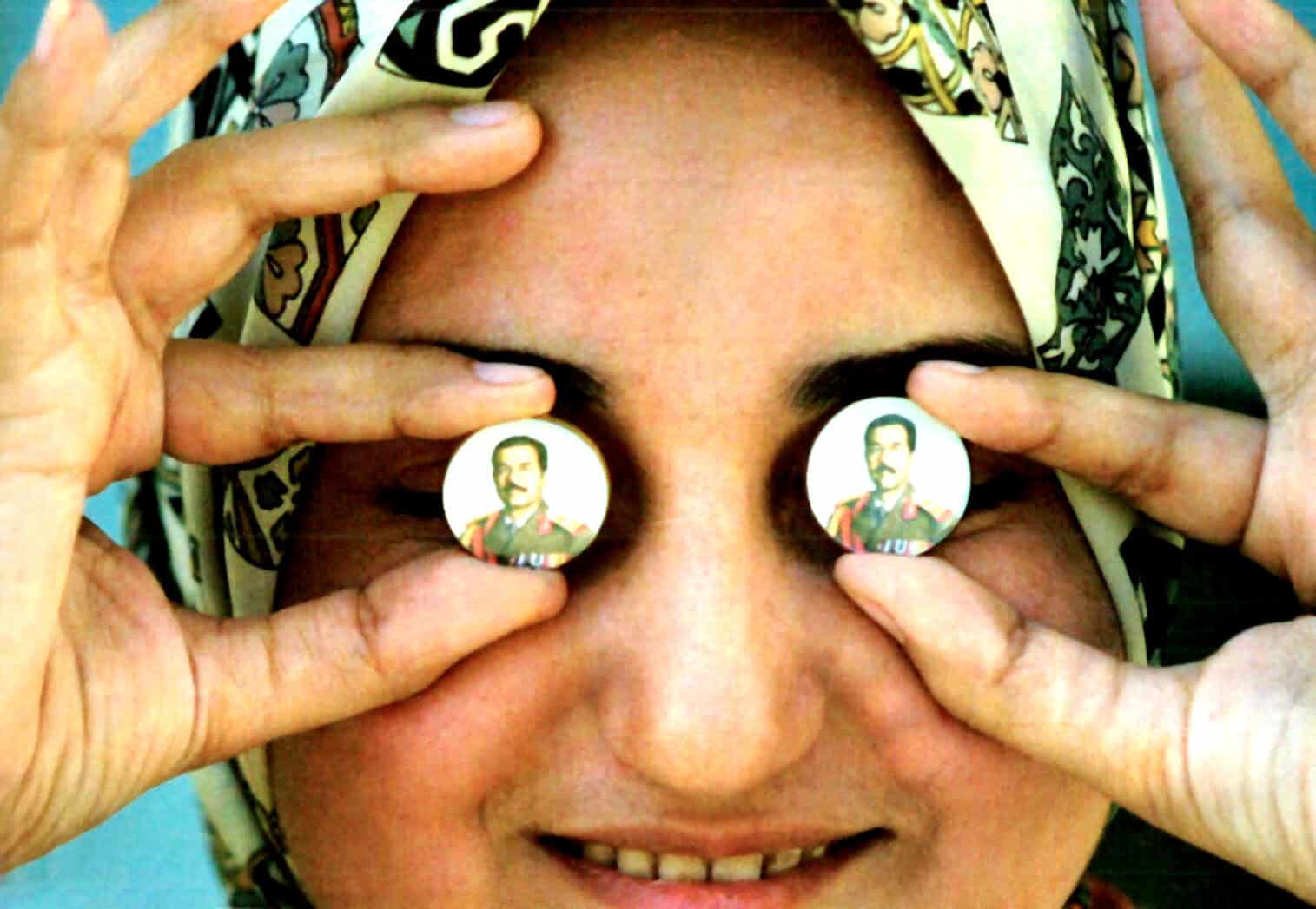 Portrait of a woman holding political campaign buttons with her eyes, promoting a historic figure, in a colorful headscarf. The image emphasizes political history and cultural expression.