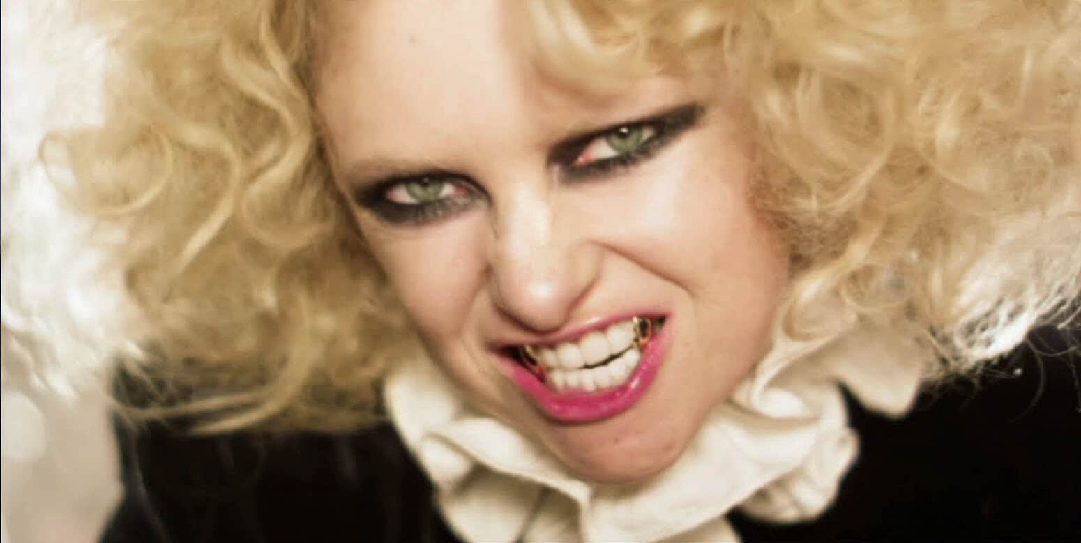 Terrifying woman with blonde curly hair and fierce expression, snarling and showing teeth, horror style, dark makeup, intense close-up for music, news, and history archives on Past Daily.
