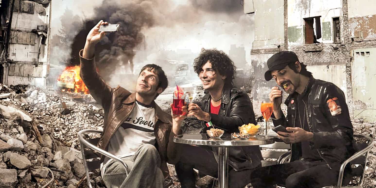 Smiling men enjoying drinks and taking selfies amidst destruction and smoke, highlighting resilience and social moments in a disaster zone for historical or news-related content.