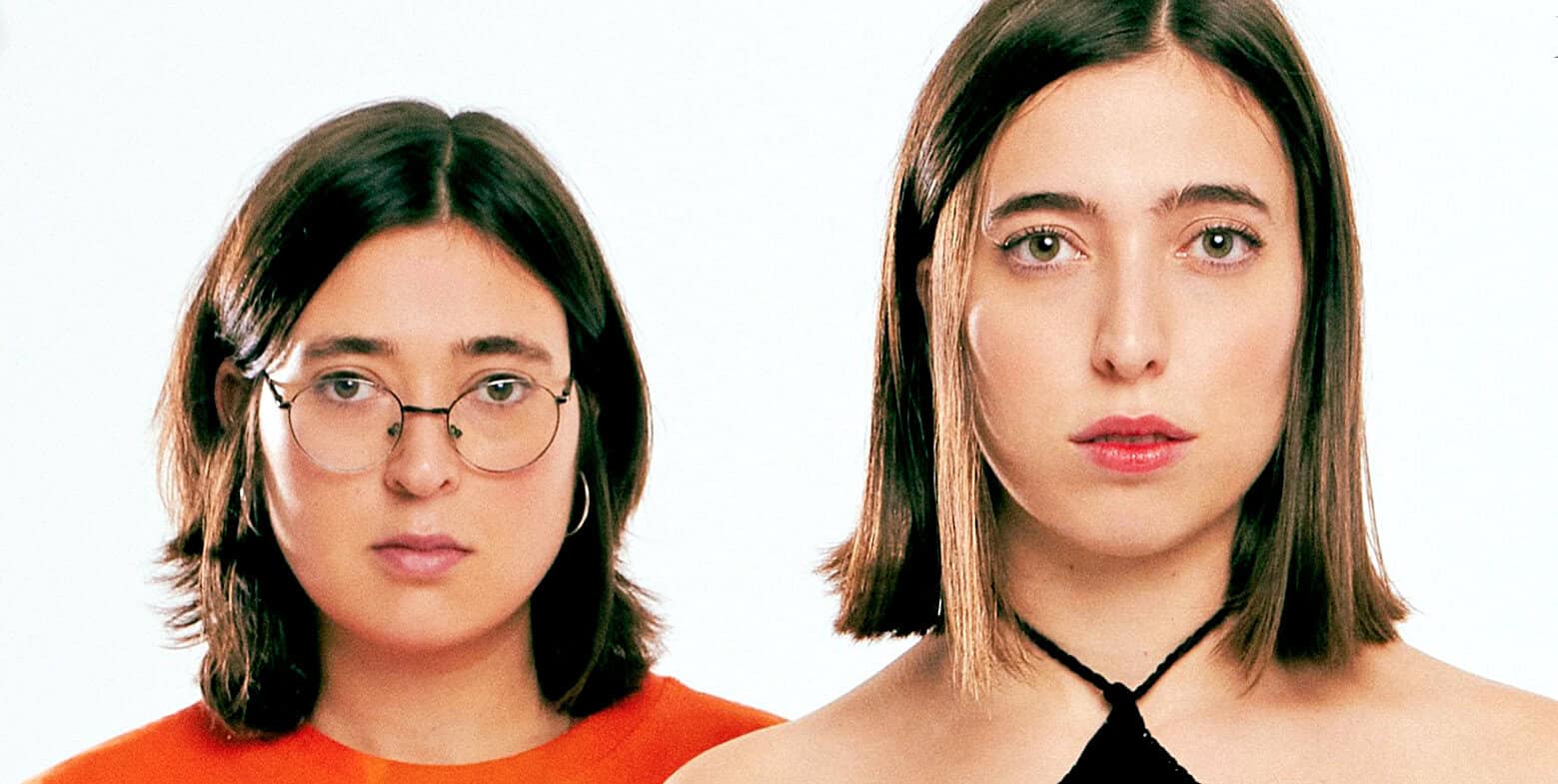 Close-up of two young women with different hairstyles and fashion styles, representing modern youth culture, film and music influences, engaging with the past daily sound archive of news, history, and music.