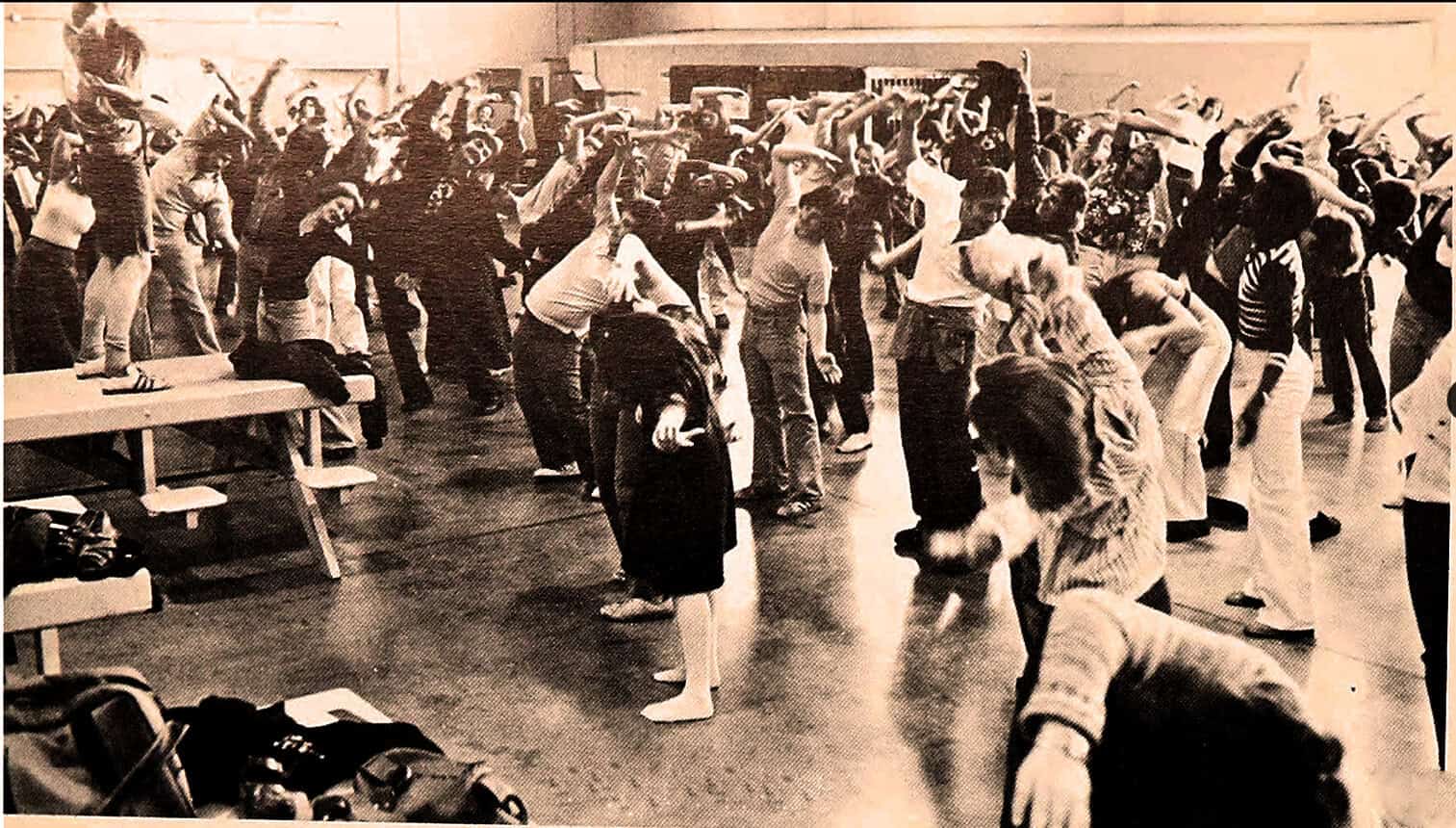 Children and adults practicing yoga poses in a large indoor space, promoting wellness, mindfulness, and community engagement in a vintage setting.