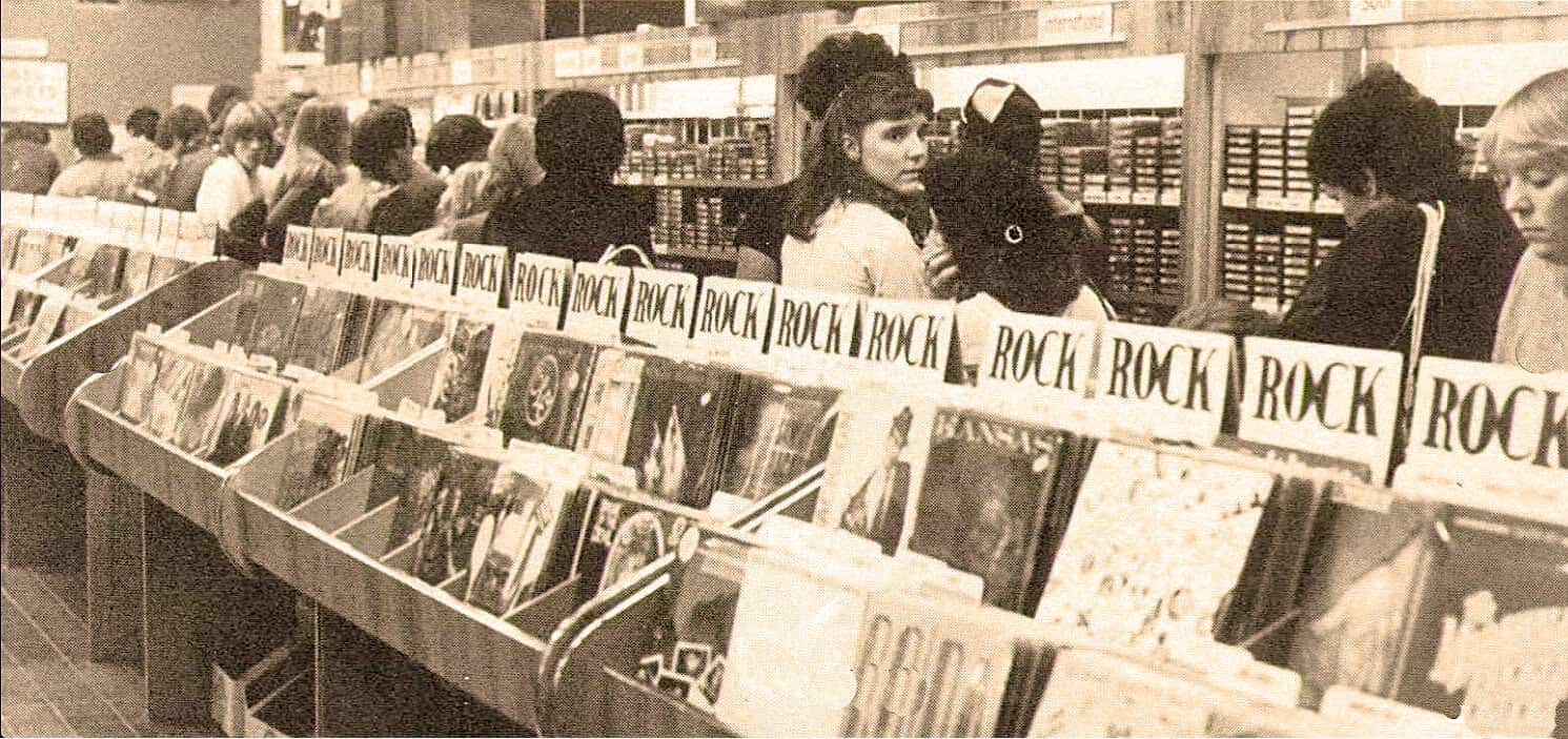 Vintage record store with people browsing rock albums, nostalgic music shopping scene from past daily archives, black-and-white photo capturing music enthusiasts and vinyl collection, historical music retail environment.