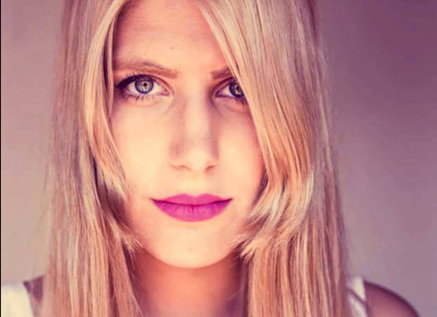 Close-up portrait of a woman with long blonde hair, blue eyes, pink lipstick, and subtle makeup, reflecting classic beauty and elegance, suitable for music and news archive visuals.