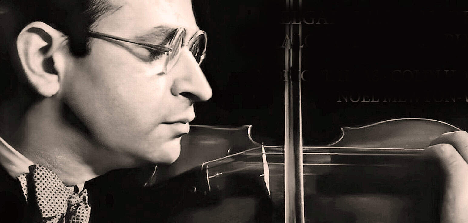 A close-up black and white photo of a man with glasses playing the violin, capturing a moment of concentration and musical artistry.