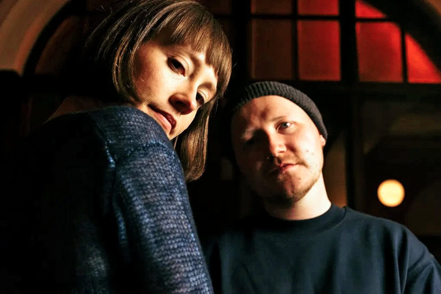 Close-up of a woman and a man indoors, showcasing a documentary or interview setting, emphasizing storytelling, human connection, and media production.